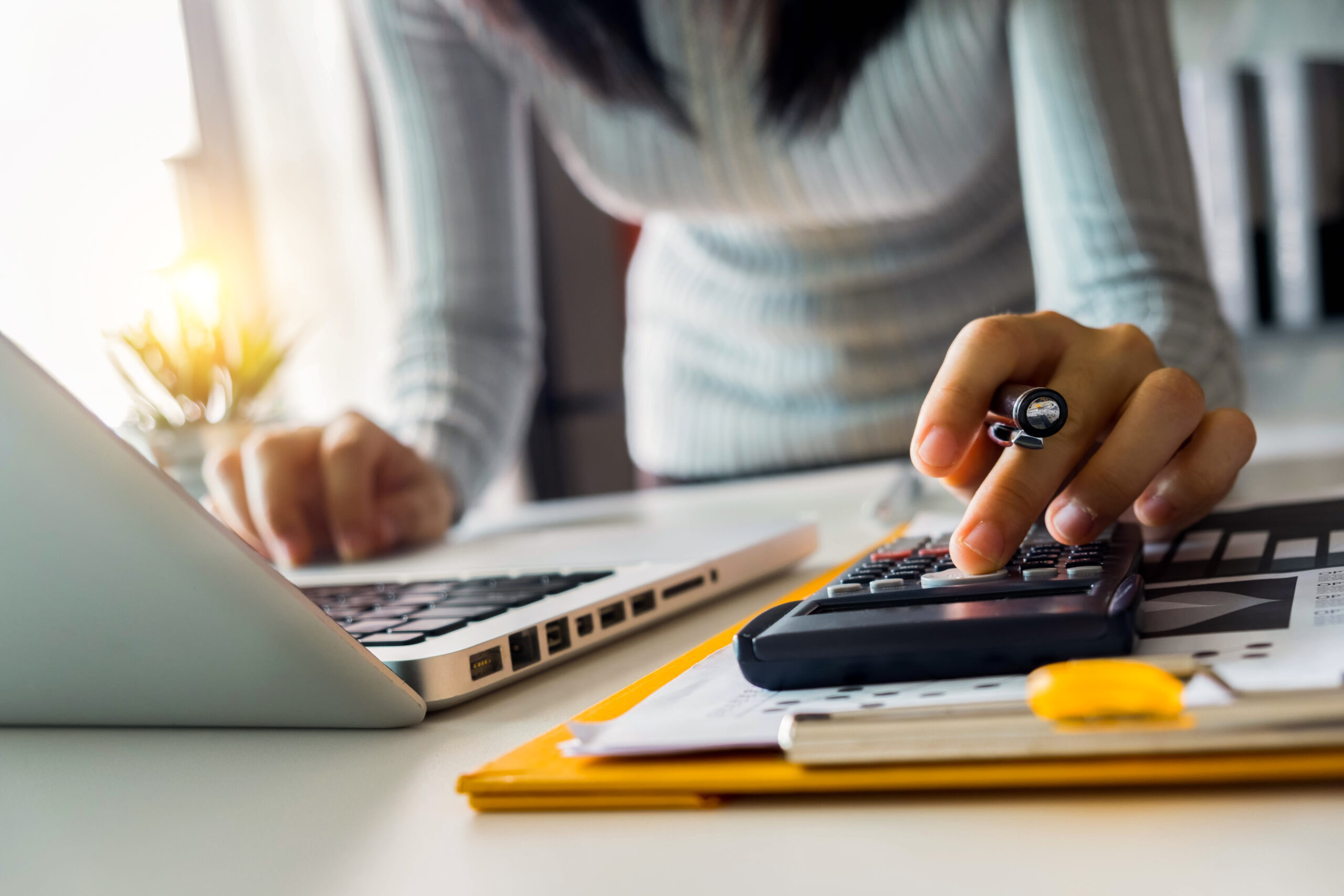 Person typing on laptop while using calculator