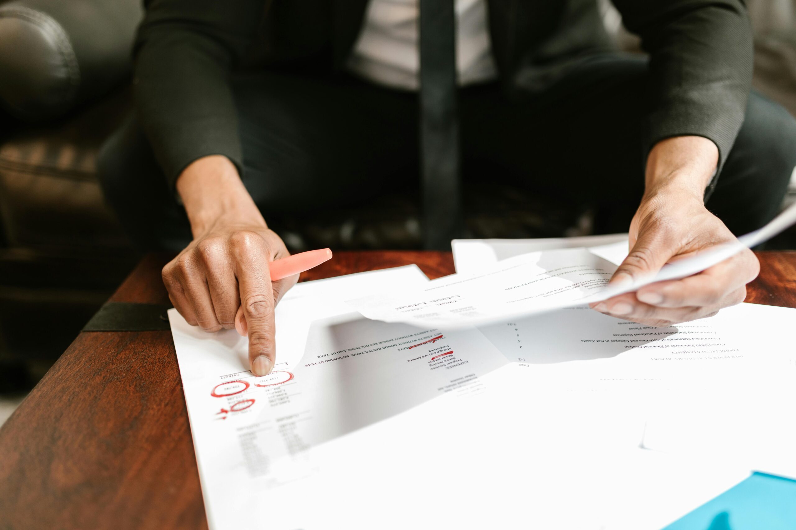 Business dressed person holds a page of a document while pointing at a red circled area on a different page.